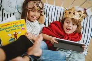 Two small kids laying in a bed reading a book and watching a Vook together