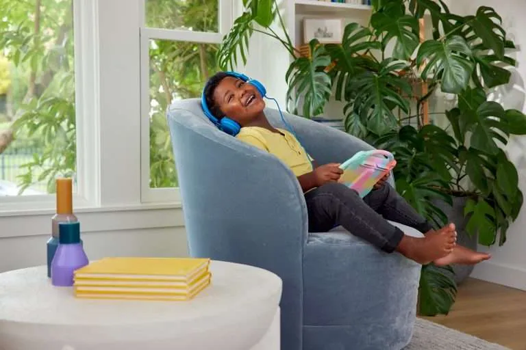 Boy sitting on chair wearing headphones and holding tablet